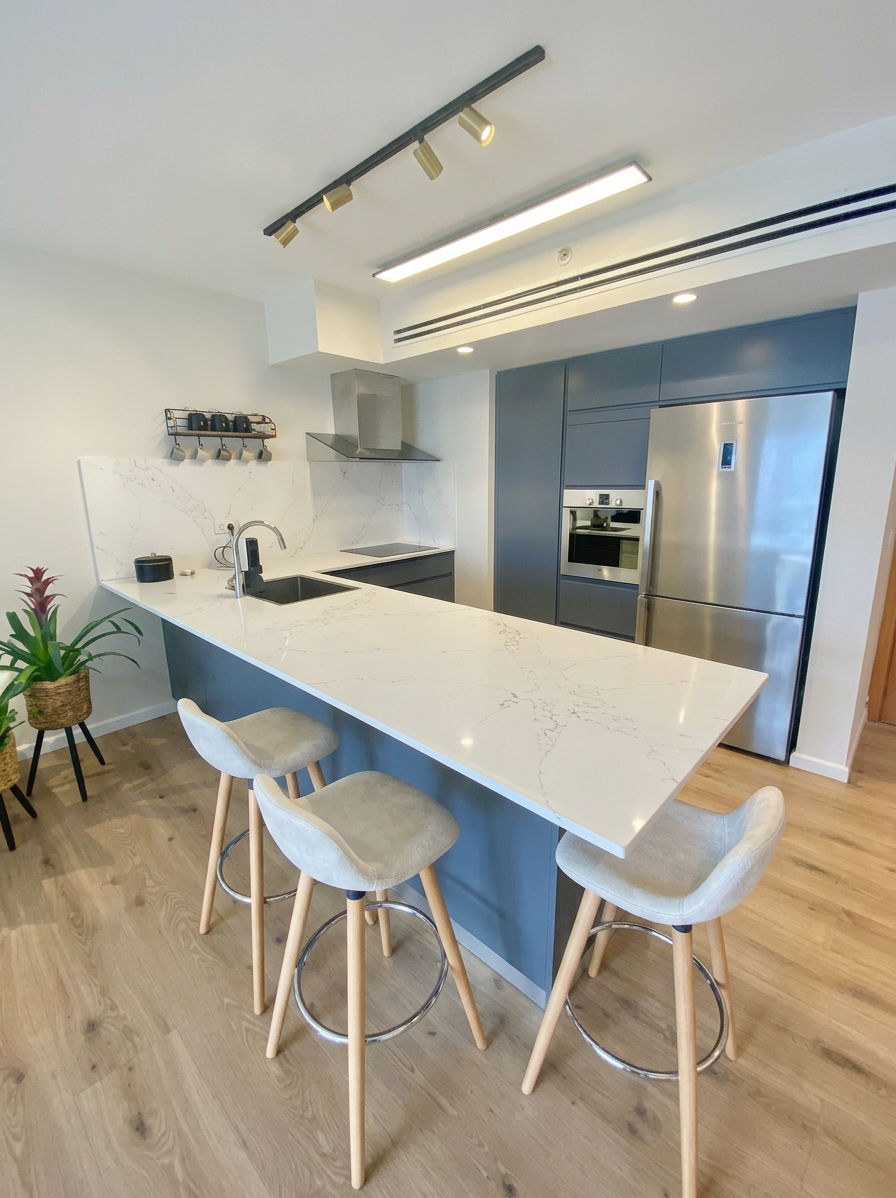 Modern kitchen with white marble countertops, a navy blue island and warm wood flooring