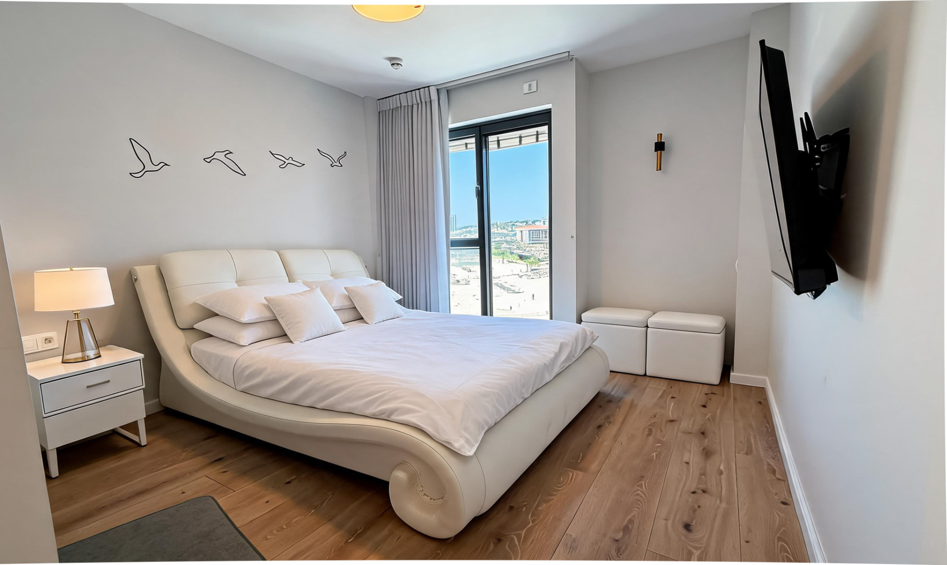 Master bedroom with a curved white bed and a window overlooking the marina coastline