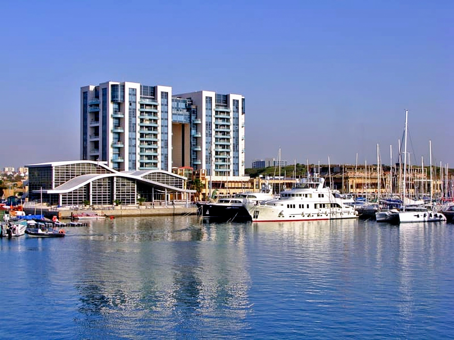 Herzliya Marina waterfront residential towers seen across the water with superyachts moored at sunset