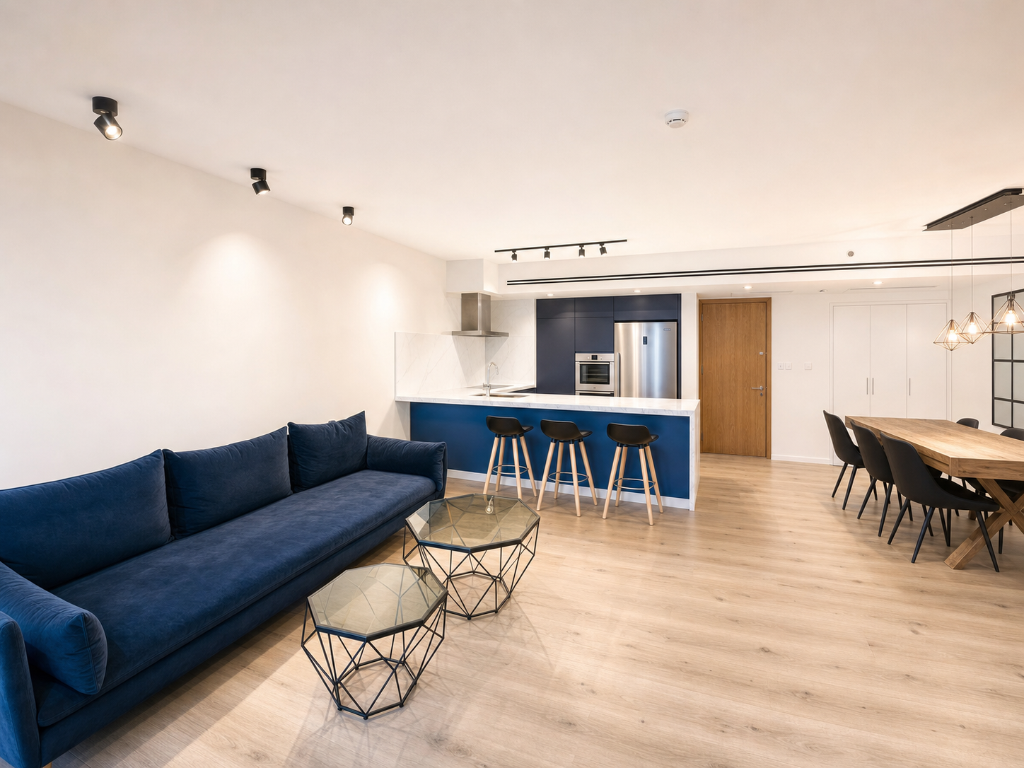 Open-plan living and dining room with a navy sofa and marina-view kitchen behind